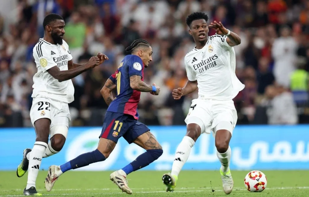 Cronología de Real Madrid contra FC Barcelona: Raphinha del Barça disputa el balón con Tchouaméni y Rüdiger del Real Madrid durante un Clásico
